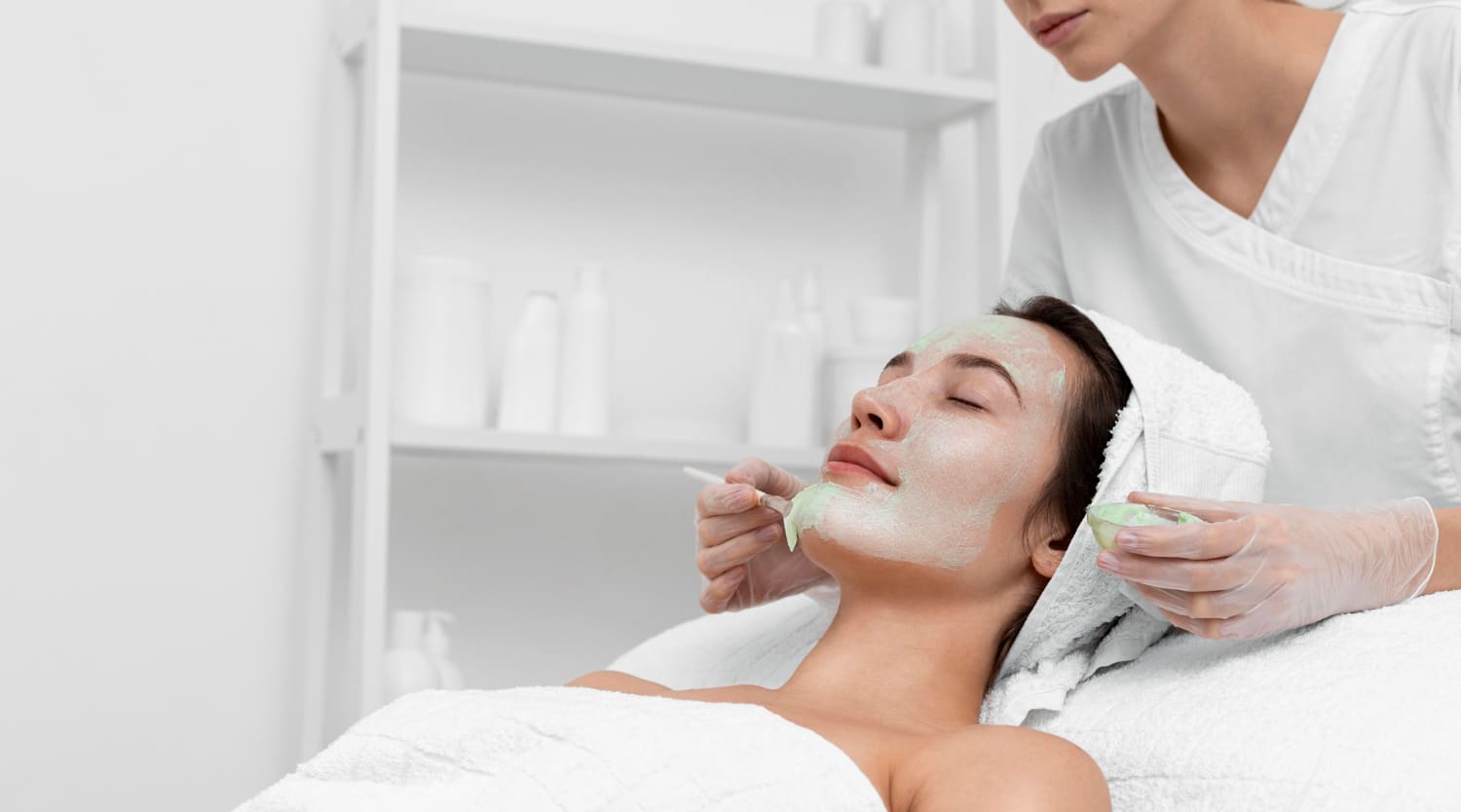 Beautician applying face mask on female client<br />
