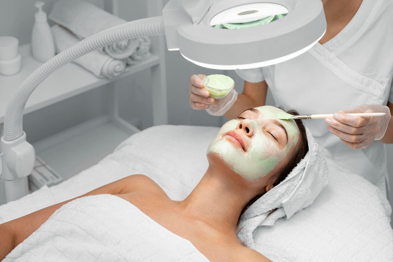 Beautician applying face mask on female client<br />
